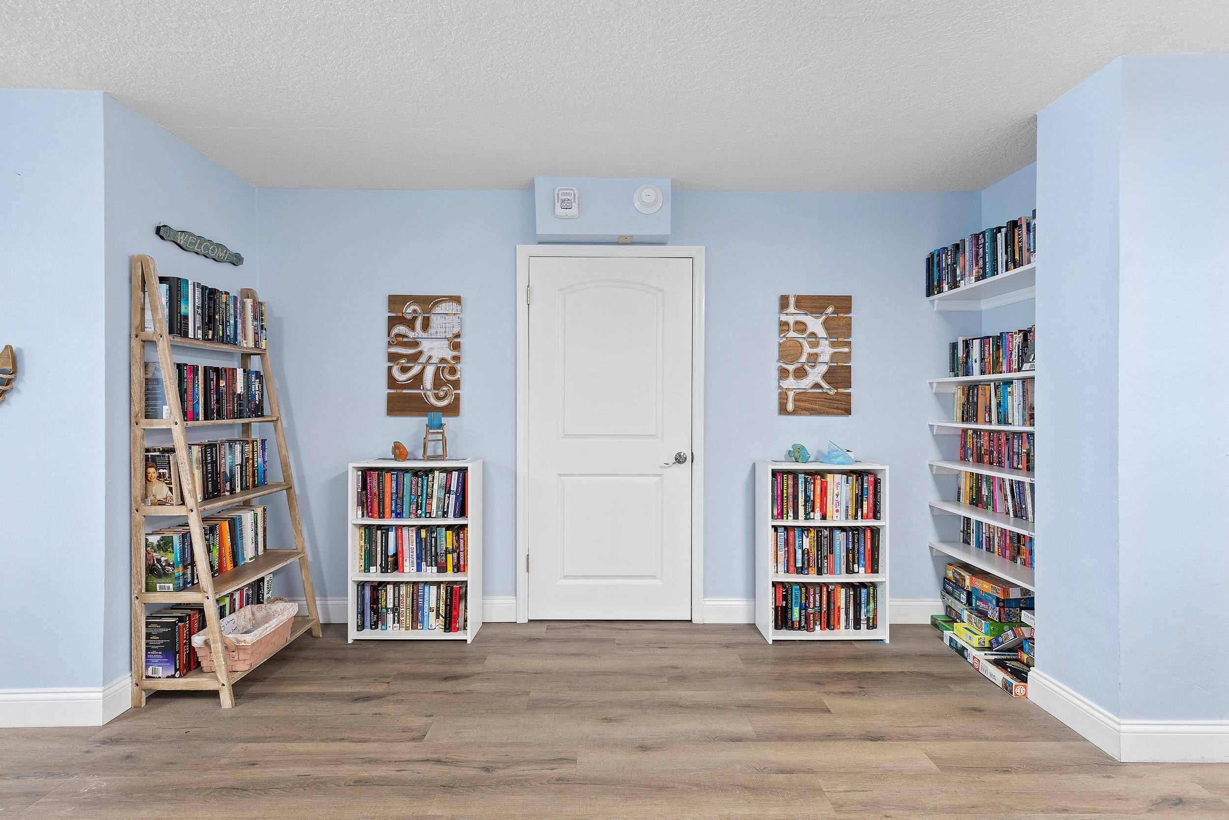 Ein Flur mit einer weißen Tür, Bücherregalen an beiden Seiten und einer hölzernen Strickleiter mit Büchern.