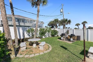 A backyard with a stone table and bench, a grill, and palm trees. - Ponce de Leon Towers 707 (New Smyrna Beach)