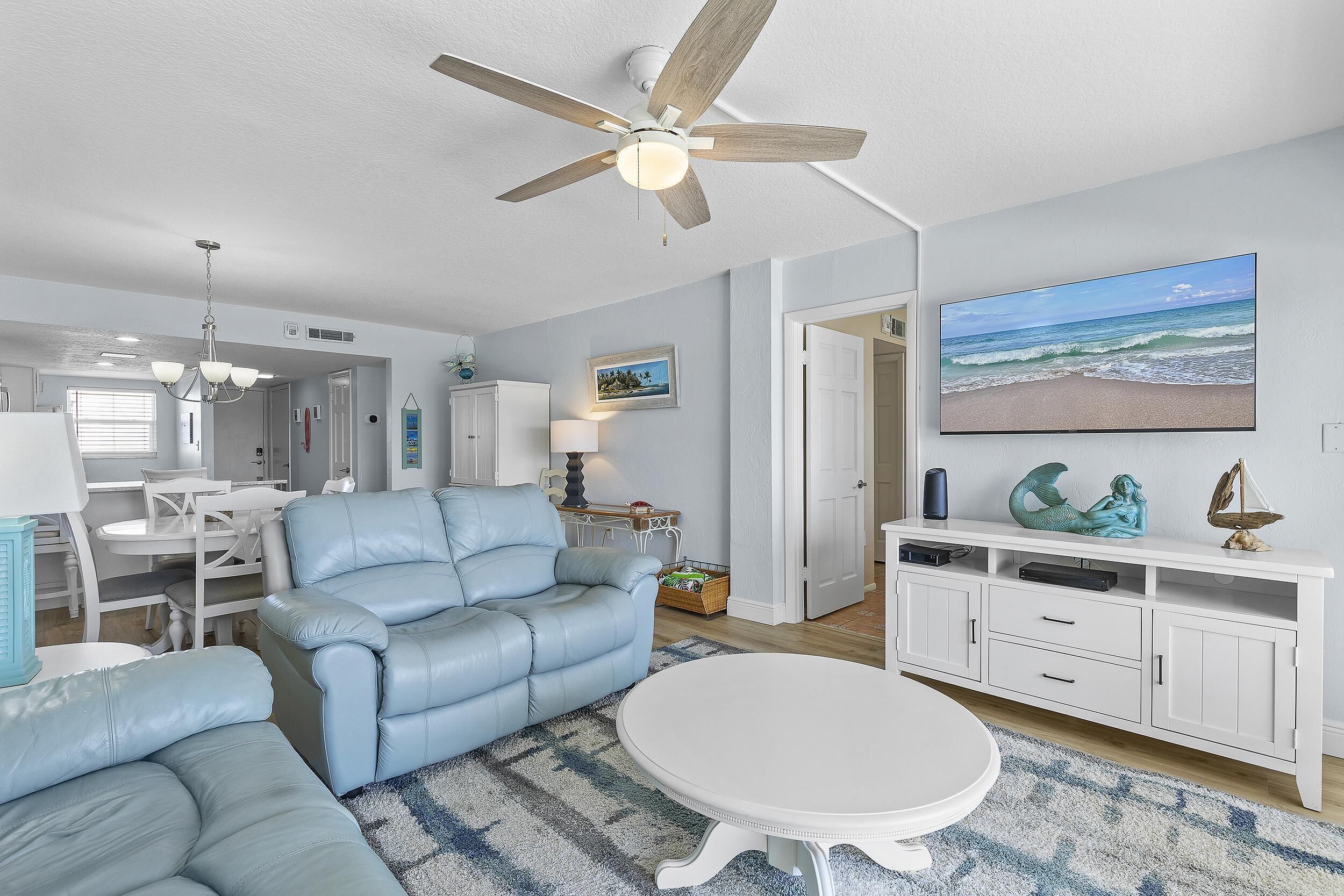 A living room with a ceiling fan, a television, a white cabinet, and a blue couch.