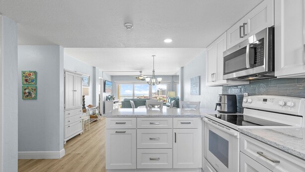 A modern kitchen with white cabinetry, a central island, stainless steel appliances, and a view to the living area. - Ponce de Leon Towers 707 (New Smyrna Beach)