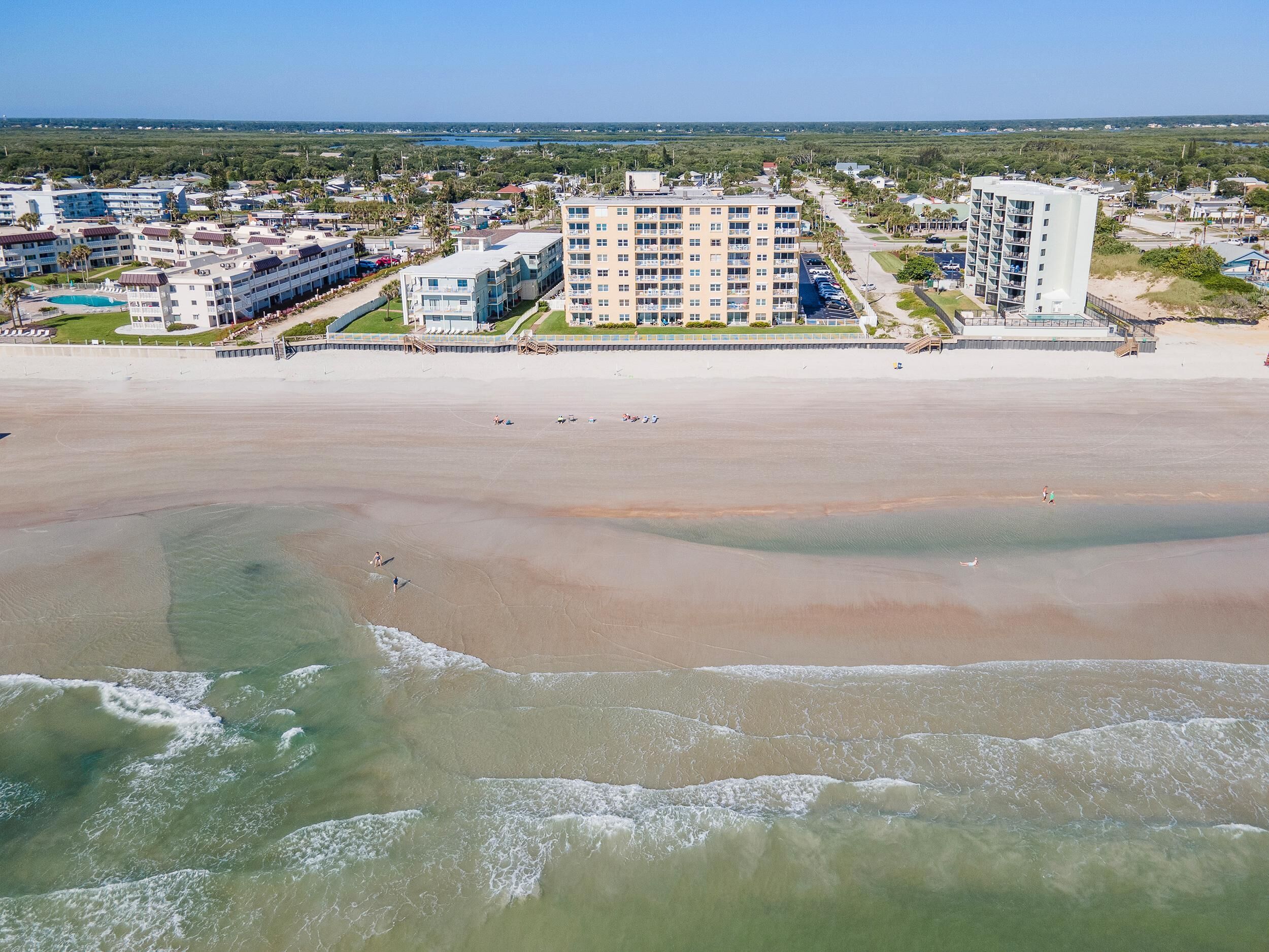 Un hotel frente a la playa con varias edificaciones, una playa arenosa y vista al océano.