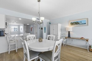 A dining area with a round table, white chairs, and a chandelier. - Ponce de Leon Towers 707 (New Smyrna Beach)