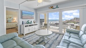 A living room with a ceiling fan, a round table, and a sofa. There is a large window with a view of the beach and a balcony with outdoor furniture. - Ponce de Leon Towers 707 (New Smyrna Beach)