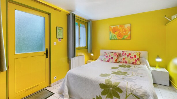 Une pièce comprenant un lit, une table de chevet, une lampe, une fenêtre avec des rideaux, un radiateur et une porte.