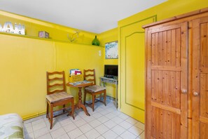 A small room with yellow walls, two wooden chairs, a small table, a wooden wardrobe, and a wall-mounted television.