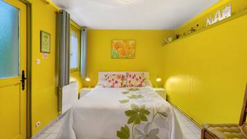 Une chambre avec un lit, deux lampes de chevet, un radiateur, une fenêtre avec des rideaux et un mur décoré d’un motif représentant un paysage urbain.