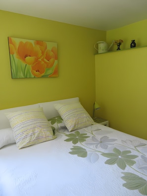Ein Bett mit floraler Bettwäsche, ein Blumenbild an der Wand und ein Nachttisch mit Tasse und Dekorationselementen.
