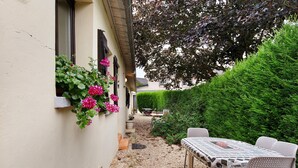 A patio area with a table and chairs, a small garden with a hedge, and a building with windows. - Guest Room 'Chambre Lecarpentier - Pensée' with Shared Terrace, Shared Garden and Wi-Fi (Fontenay)