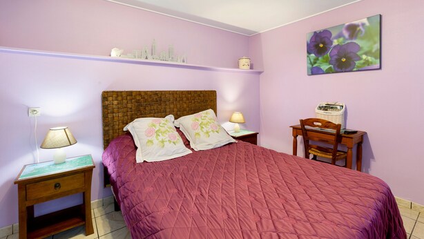 A bedroom with a single bed, a nightstand with a lamp, a wooden chair, a small table with a lamp, and a wall shelf with decorative items. - Guest Room 'Chambre Lecarpentier - Pensée' with Shared Terrace, Shared Garden and Wi-Fi (Fontenay)