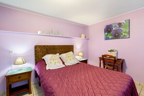 A bedroom with a single bed, a nightstand with a lamp, a wooden chair, a small table with a lamp, and a wall shelf with decorative items. - Guest Room 'Chambre Lecarpentier - Pensée' with Shared Terrace, Shared Garden and Wi-Fi (Fontenay)