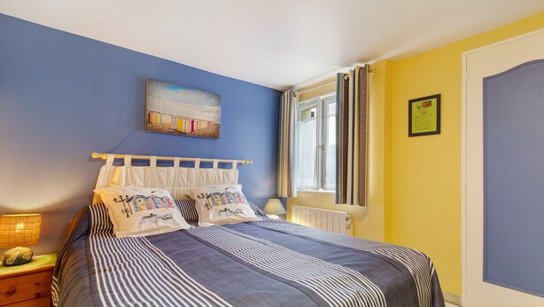 A bedroom with a bed, a nightstand, a lamp, a window with curtains, and a painting on the wall. - Family Room Lecarpentier - Coquillage (Fontenay)