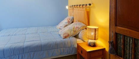 Un dormitorio con cama, mesita de noche, lámpara, una puerta y dos cuadros en la pared.