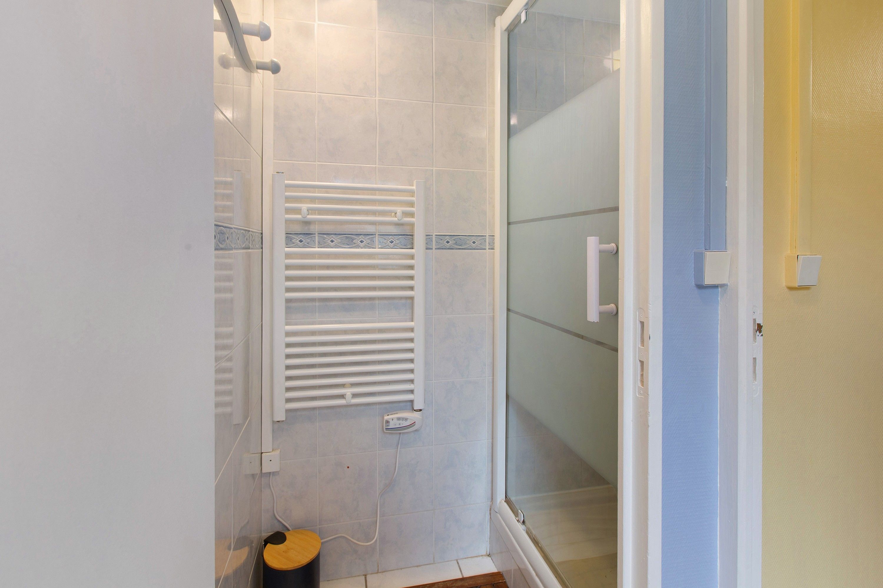 Une salle de bain avec une douche à parois de verre, un porte-serviettes blanc et un petit tabouret en bois.