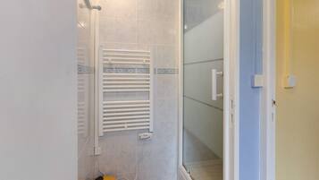 Une salle de bain avec une douche à parois de verre, un porte-serviettes blanc et un petit tabouret en bois.