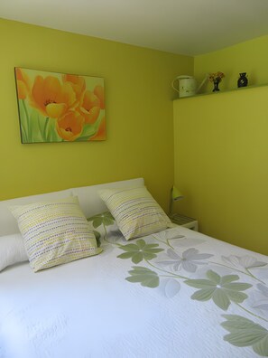 Una cama con ropa de cama floral, un cuadro de flores en la pared y una mesita de noche con una taza y objetos decorativos.