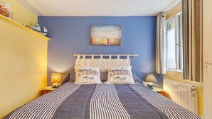 A bedroom with a bed, two pillows, a nightstand, a lamp, a window, and a painting on the wall. - Family Room Lecarpentier - Coquillage (Fontenay)