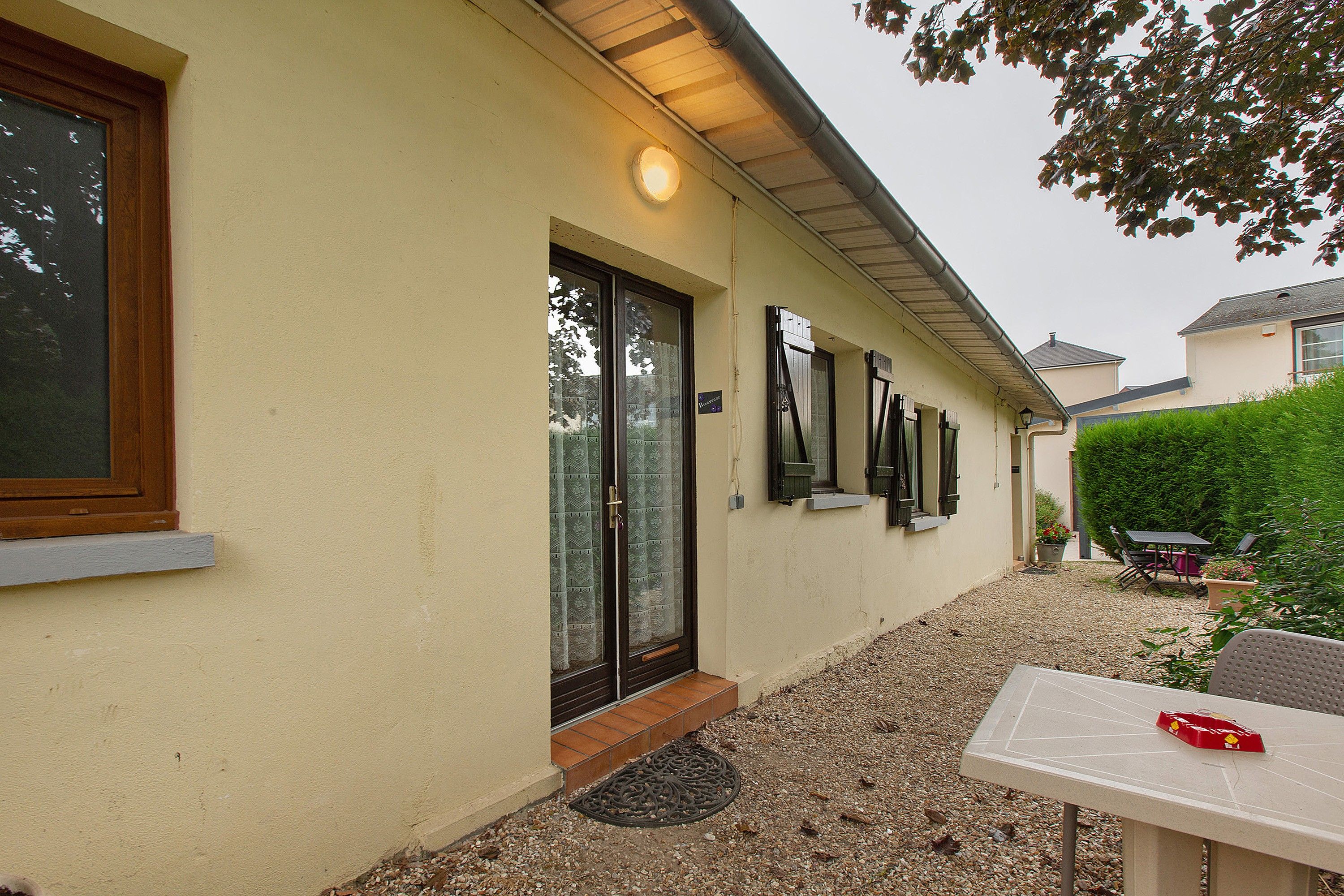 Een gebouw met een beige gevel, een deur met een ruit en een klein terras met een tafel en stoelen.