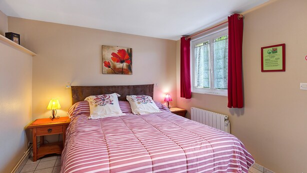 Une chambre à coucher avec un lit, une table de chevet, une lampe, une fenêtre avec des rideaux et un tableau au mur.