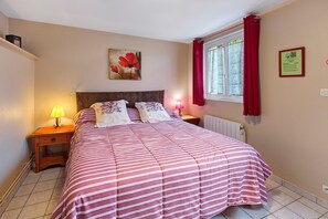 Une chambre à coucher avec un lit, une table de chevet, une lampe, une fenêtre avec des rideaux et un tableau au mur.