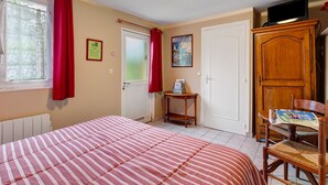 Une chambre à coucher comprenant un lit, une chaise, une table, une armoire, une porte et une fenêtre avec des rideaux.