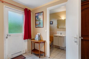 Une salle de bain avec des toilettes, un lavabo et un miroir. On y trouve une petite table avec un porte-revues.