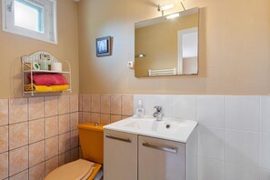 Une salle de bain avec des toilettes, un lavabo et une étagère où sont rangées les serviettes.