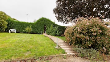 A pathway leading to a building entrance, surrounded by well-maintained hedges and a grassy area with a bench.