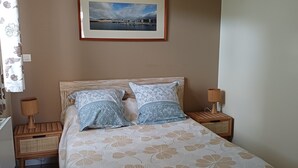 Une chambre à coucher avec un lit, deux tables de chevet, une lampe, un tableau encadré au mur et un rideau.