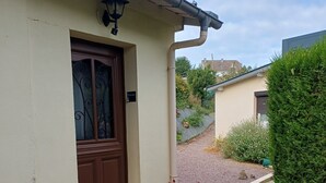 Une terrasse avec une table et des chaises, une porte avec une fenêtre, et un petit espace jardin aménagé avec du gravier et des plantes.