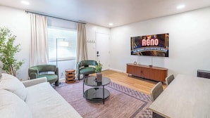 A modern living room with a sofa, two chairs, a round coffee table, a TV, and a wooden cabinet.