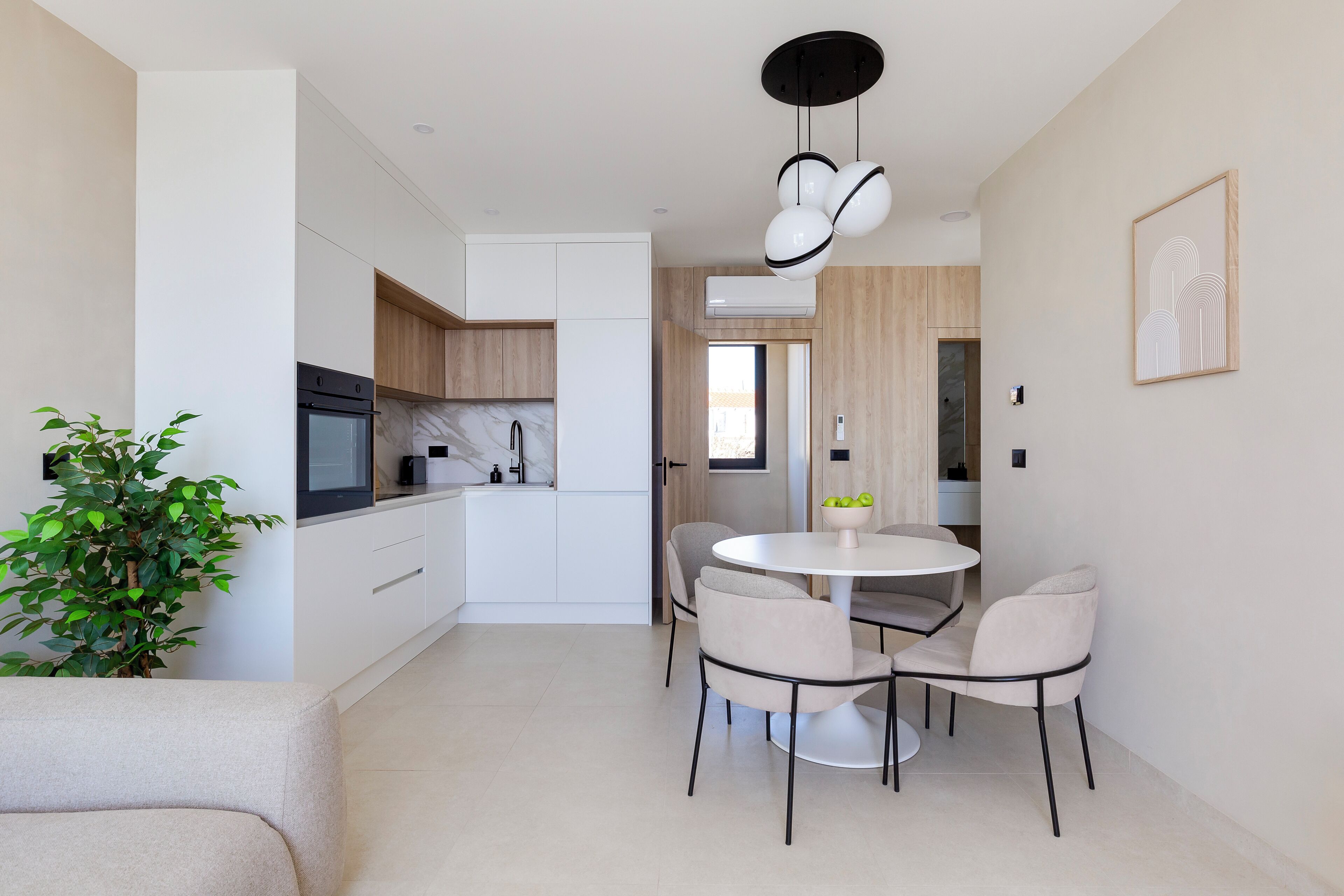 A modern kitchen with white cabinets, a built-in oven, and a dining area with a round table and four chairs.
