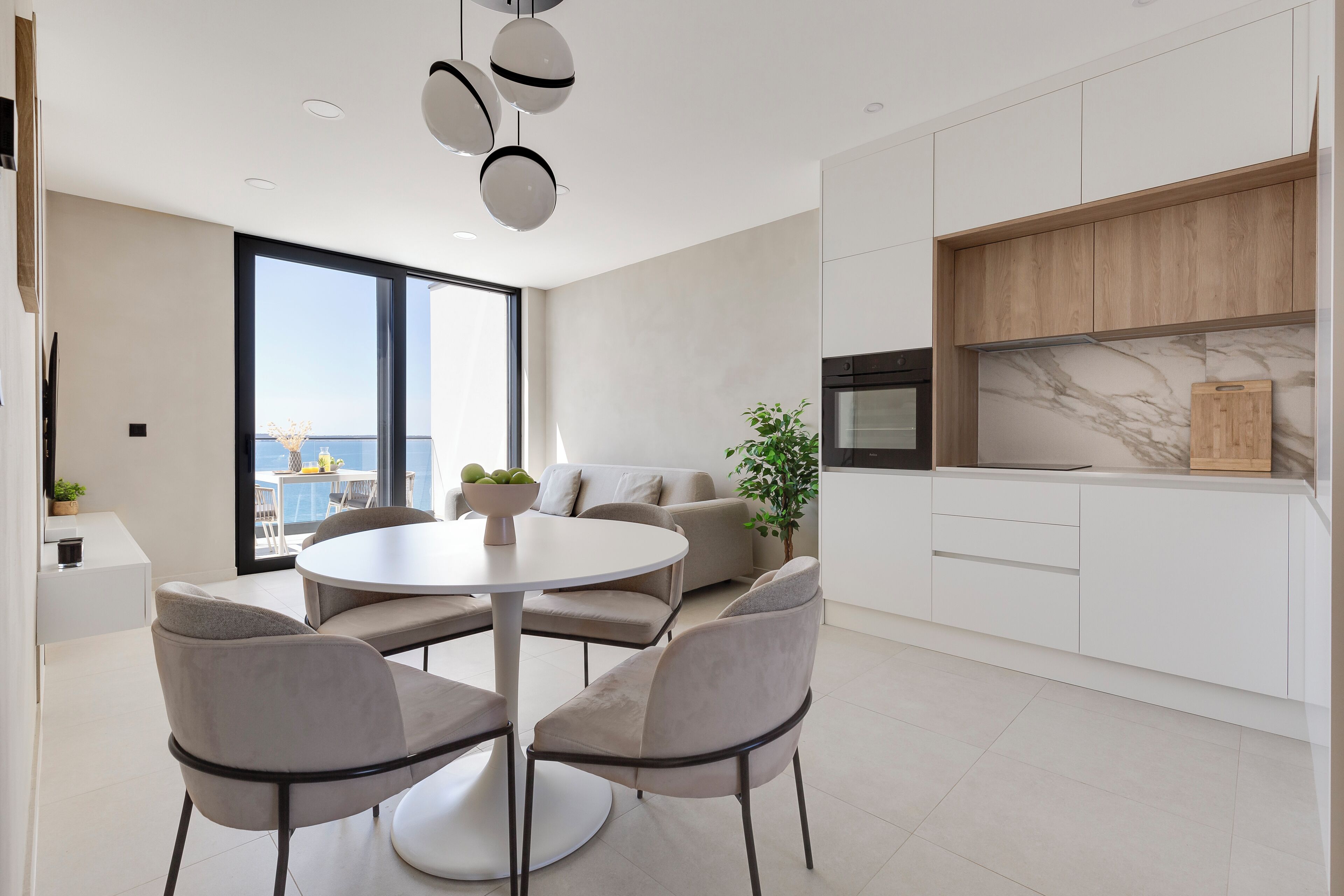 A modern kitchen with white cabinets, a marble backsplash, and a round dining table with four chairs.