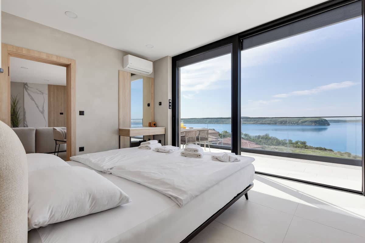 A modern bedroom with a large bed, a desk, and a view of a lake.