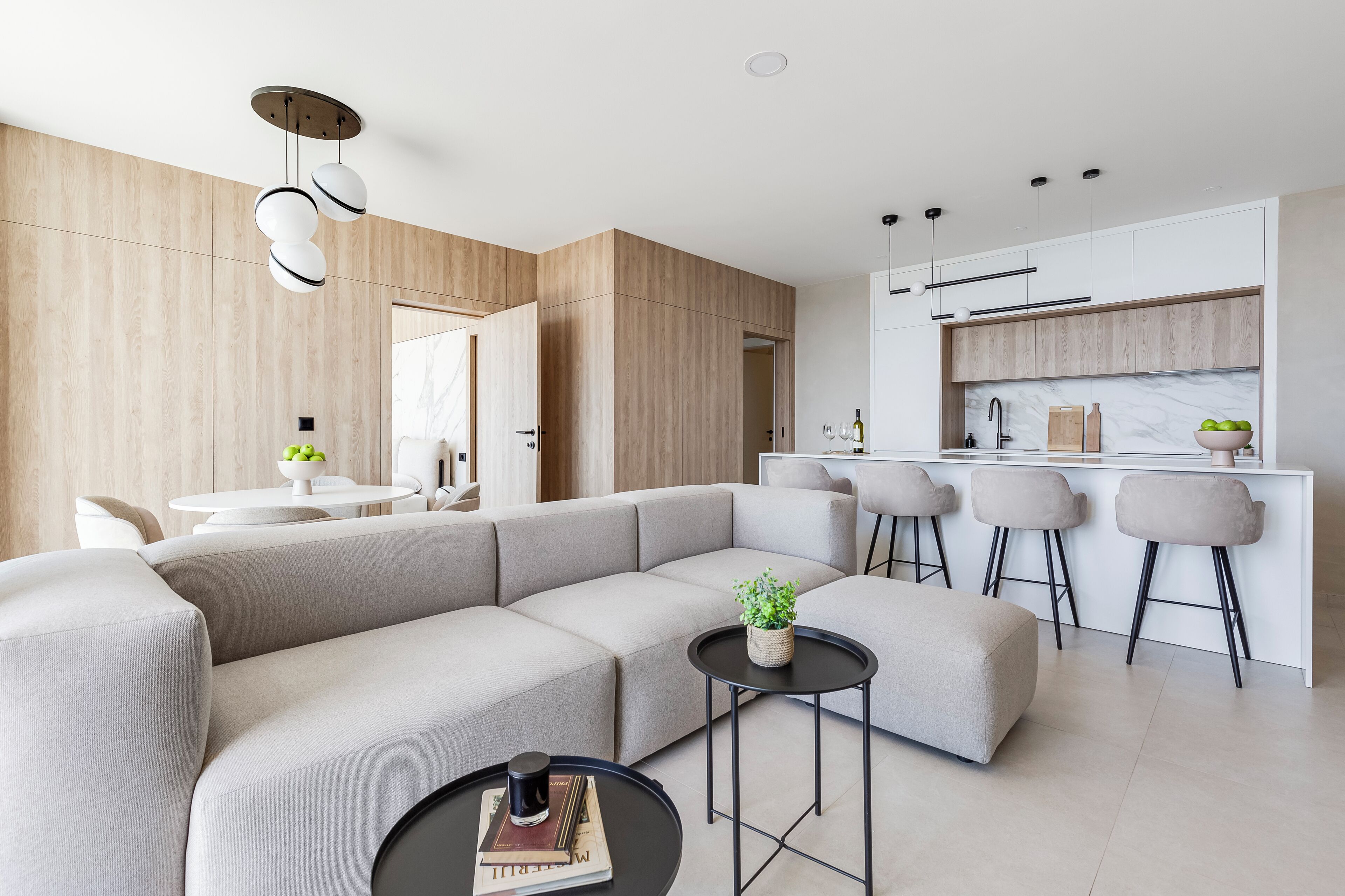 Una sala de estar moderna con un sofá seccional, un comedor con una mesa redonda y una cocina con taburetes de bar.