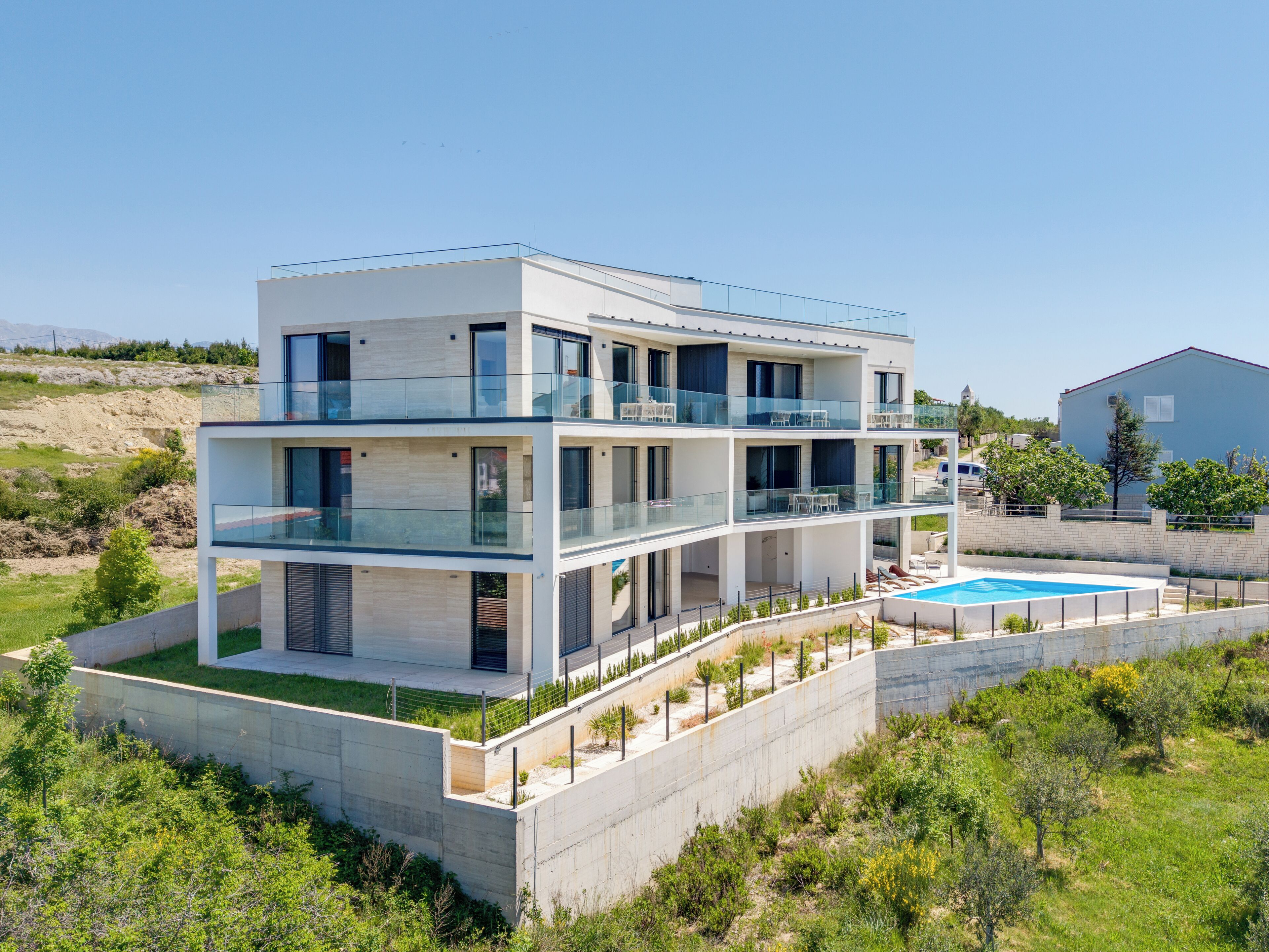 A modern multi-story residential building with a glass balcony, a swimming pool, and a landscaped garden.