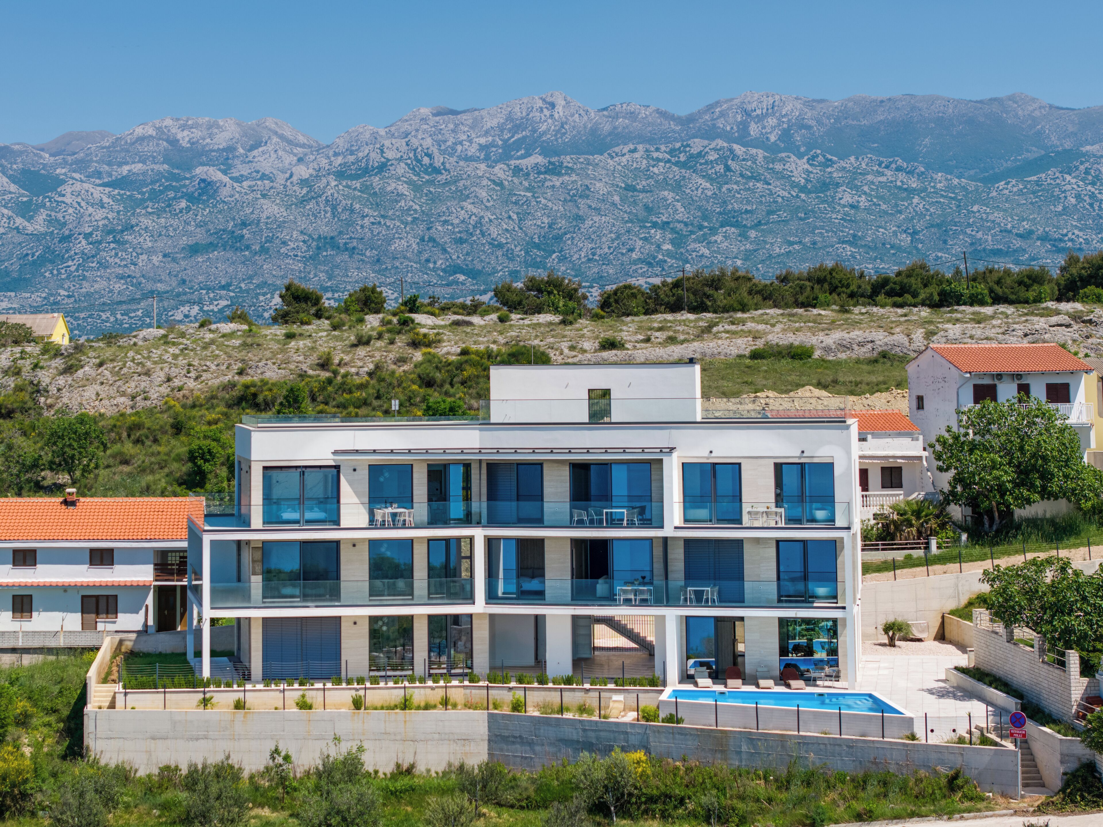 Un edificio moderno de varios pisos con piscina, rodeado de un paisaje montañoso.