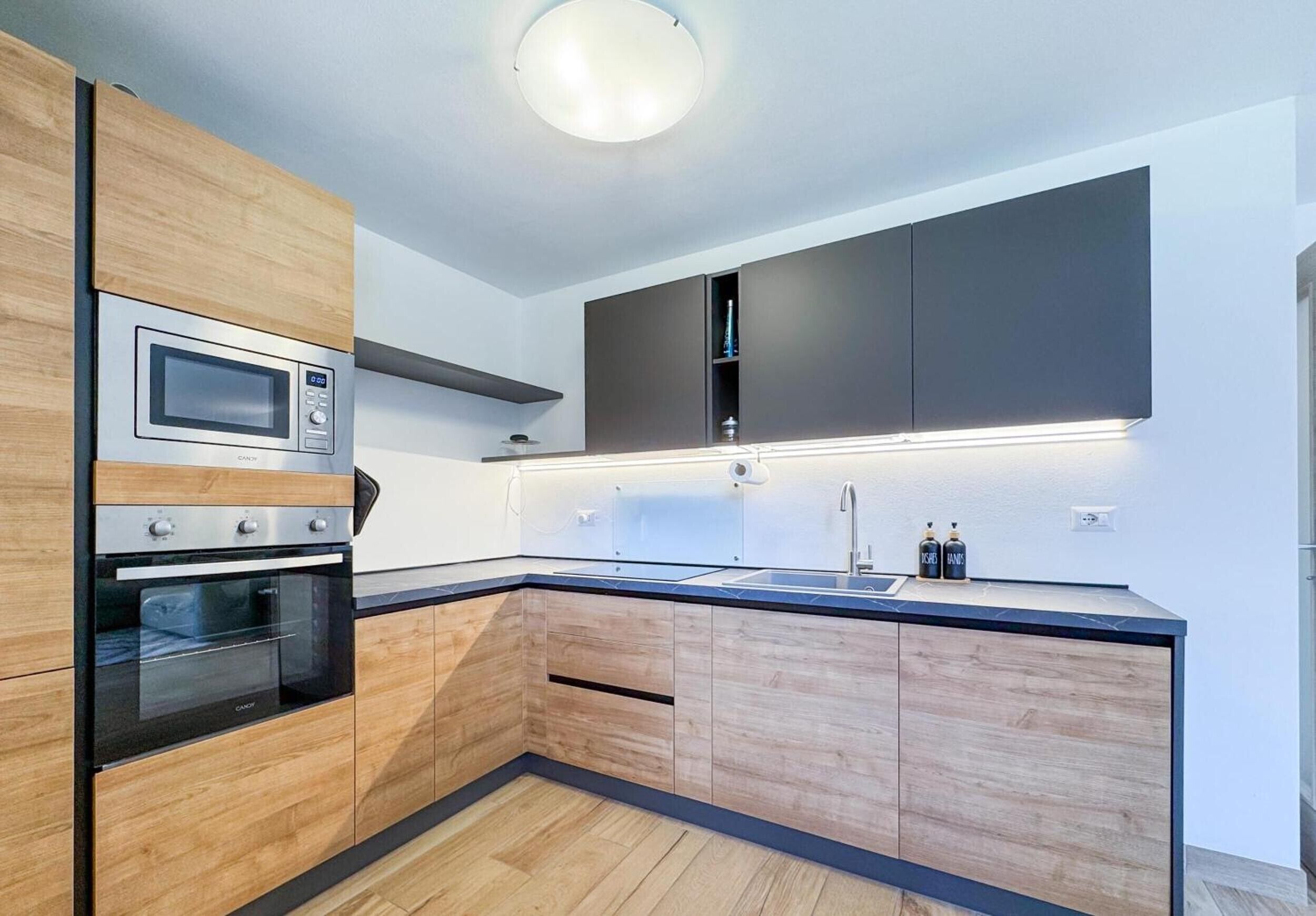 A modern kitchen with built-in appliances, wooden cabinetry, and a black countertop.