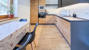 Una cucina compatta con mobili in legno, un forno a microonde e un lavandino. C'è un tavolo da pranzo con sedie e una pianta in vaso vicino alla finestra.