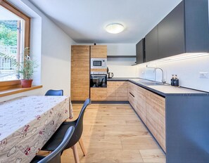 Une cuisine compacte avec des meubles en bois, un four à micro-ondes et un évier. On y trouve une table à manger avec des chaises, ainsi qu’une plante en pot près de la fenêtre.