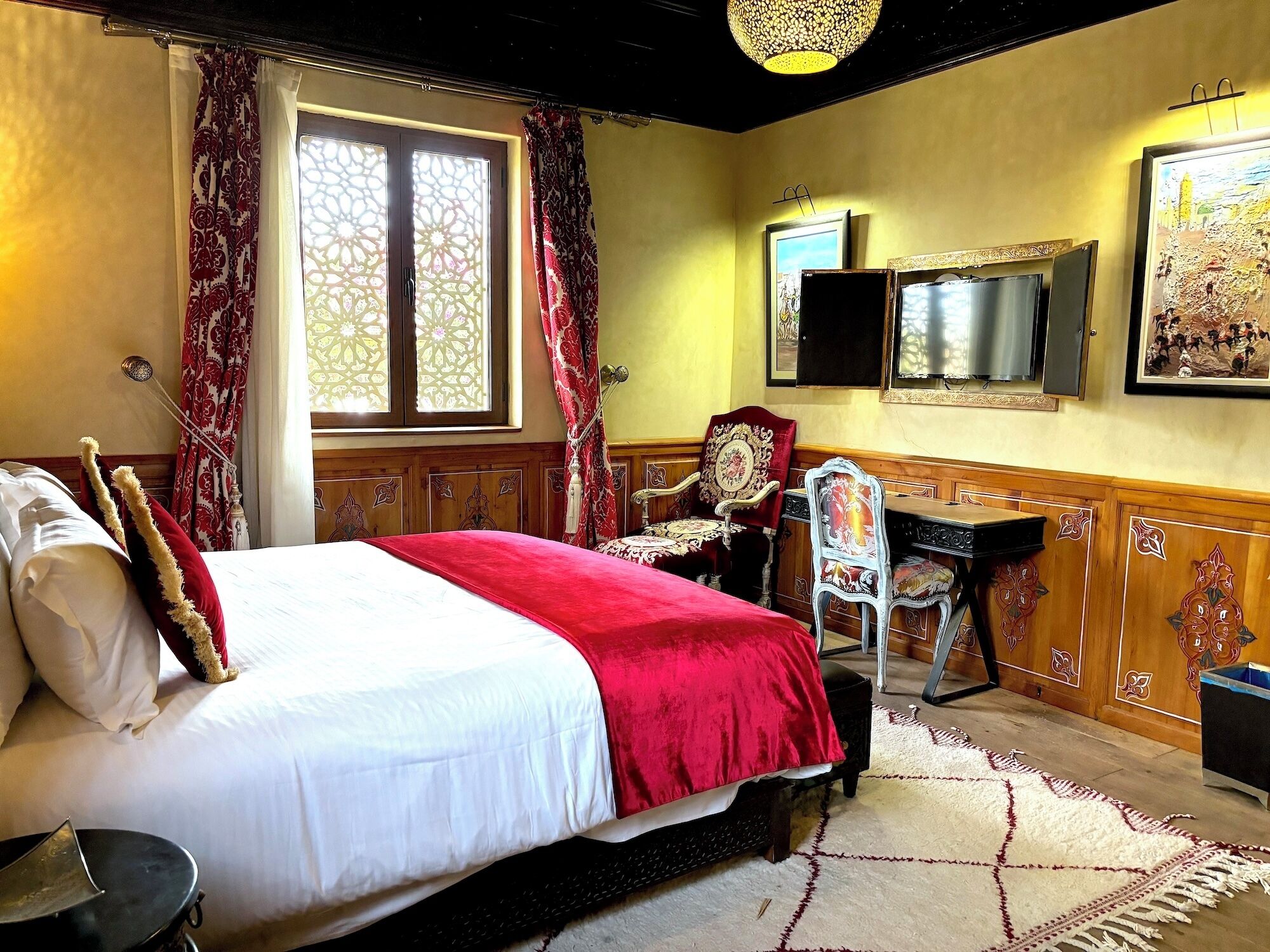 A hotel room with a large bed, a desk, a chair, a mirror, and a window with curtains.