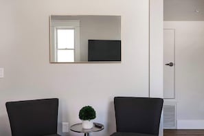 A room with two black chairs, a small table with a potted plant, a wall-mounted mirror, and a door. - The Penn Hotel - Hip 2BR Suite in Central Gaslamp Walk Score 99! (San Diego)