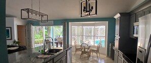 A modern kitchen with a large island, a dining area with chairs, a chandelier, and a view through the windows. - Villa Agualinda canal home with heated pool (Cape Coral)