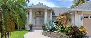 A residential house with a front porch, a garage, and a well-maintained garden with various plants. - Villa Agualinda canal home with heated pool (Cape Coral)
