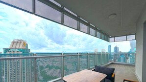 Un balcón con vistas a un horizonte urbano, una mesa de madera y sillas negras.