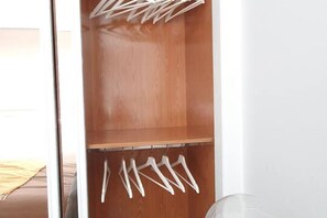 Un placard en bois avec des cintres blancs et une porte en verre transparent.