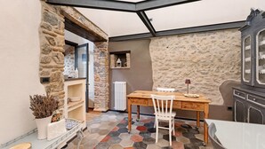 A corner room with a stone wall, a wooden table with chairs, a radiator, and a cabinet.