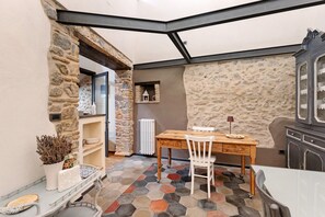 Ein Eckzimmer mit Steinwand, einem Holztisch mit Stühlen, einem Heizkörper und einem Schrank.
