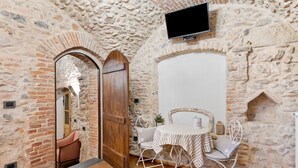 A stone-walled room with a wooden door, a table with chairs, and a mounted television.