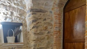 A stone-walled room with a wooden door, a small window with a basket, and a pink upholstered chair.