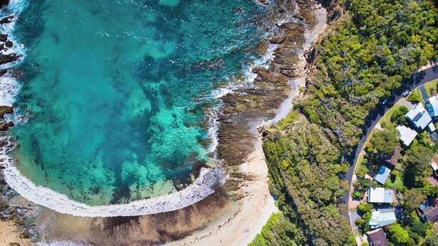 An aerial view of a coastal area with a beach, rocky shoreline, and a residential area with houses.